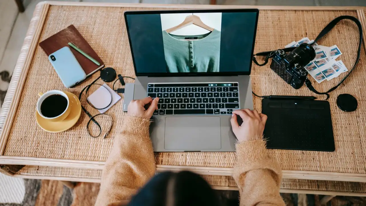 Vue du dessus d'un bureau avec ordinateur portable affichant une photo de vêtement, appareil photo et café