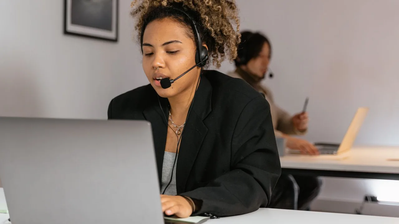Une employée du support client avec un casque-micro, concentrée devant son ordinateur portable dans un bureau.