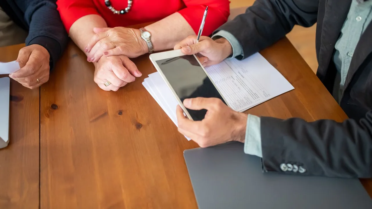 Des mains autour d'une tablette et d'un formulaire posés sur une table en bois lors d'une réunion