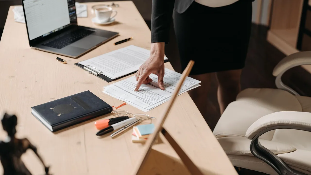 Une femme penchée sur un bureau pointe du doigt un document, ordinateur portable et stylos à côté