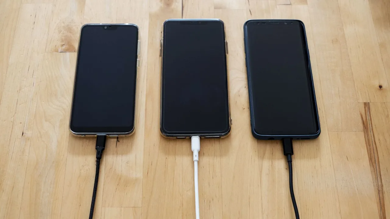 Trois smartphones branchés à des câbles de charge, alignés sur une table en bois clair