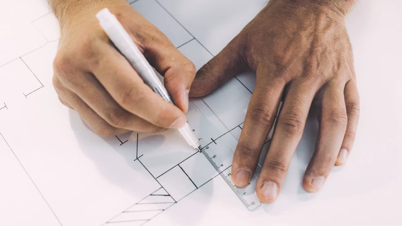 Mains traçant un plan à la règle graduée et au stylo sur une feuille blanche