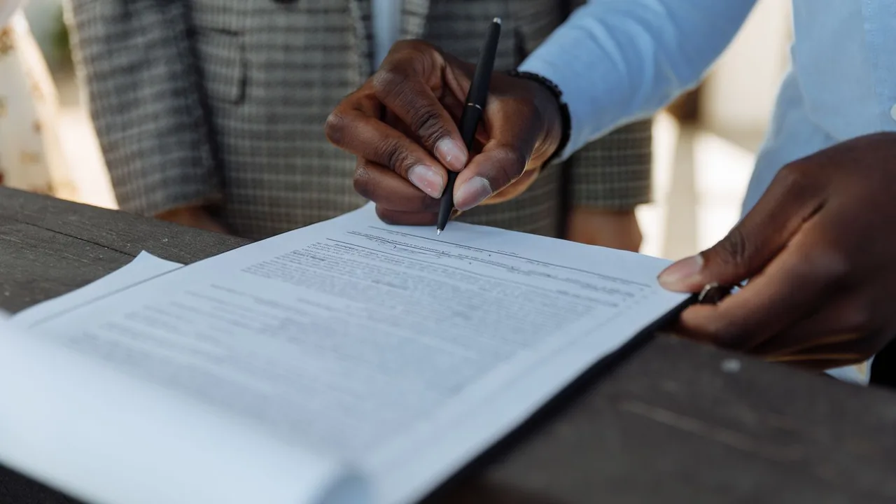 Gros plan de mains qui signent un document avec un stylo sur un bureau sombre