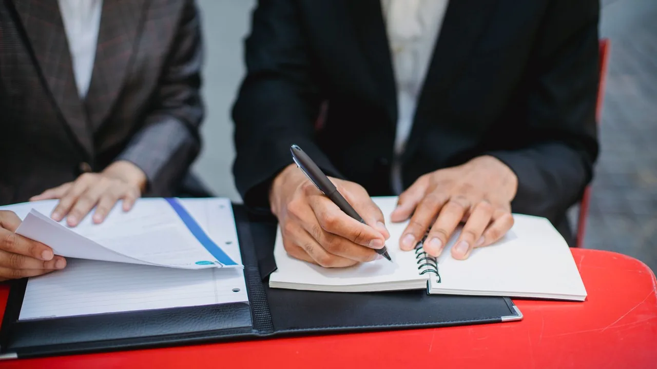 Mains qui prennent des notes dans un carnet posé sur un porte-documents noir