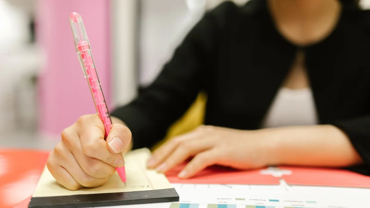 Une femme écrit au stylo rose sur un bloc de notes, des graphiques colorés posés devant elle
