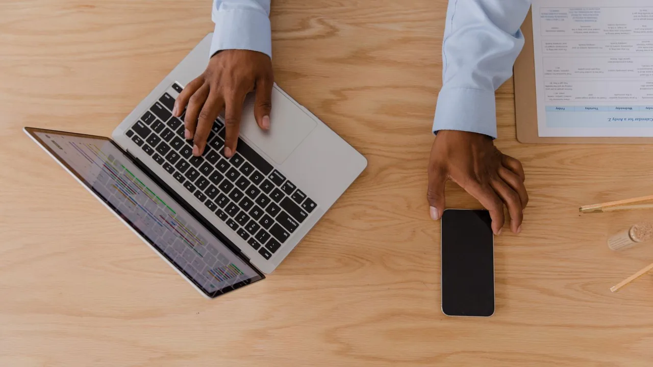 Vue de dessus : mains sur un ordinateur portable ouvert, un smartphone posé sur un bureau en bois clair