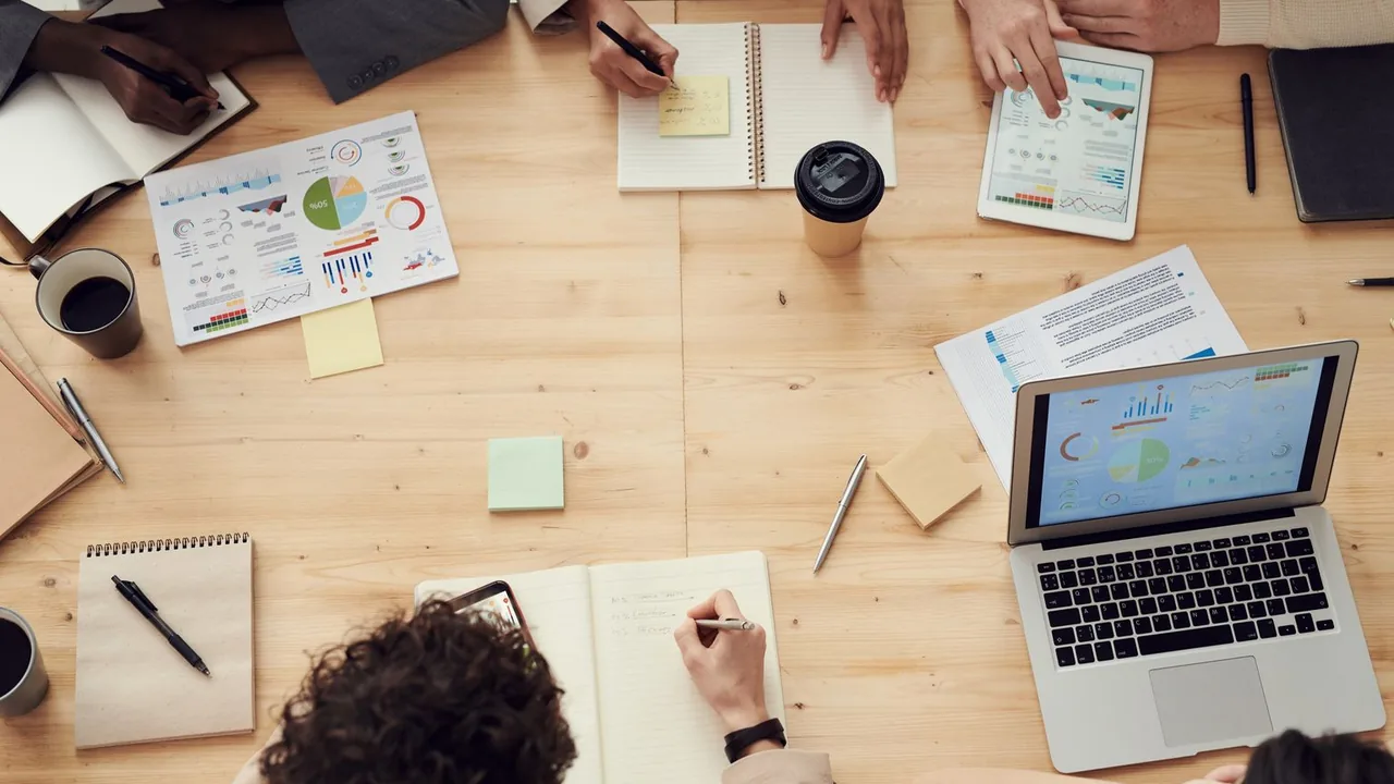 Vue de dessus d'une table de réunion : carnets, graphiques imprimés, tablette et ordinateur portable