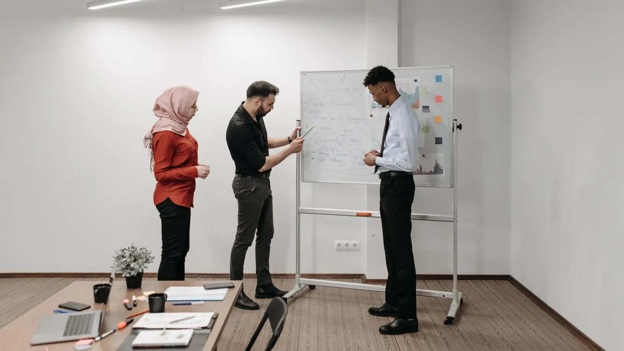 Trois professionnels préparent un projet devant un tableau blanc dans une salle lumineuse