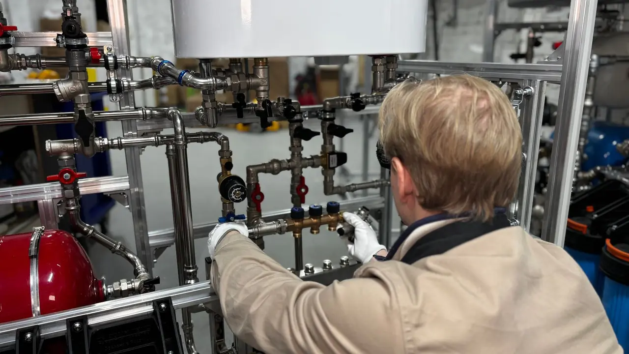 Technicien de dos, gants blancs, réglant une tuyauterie industrielle avec vannes et compteurs