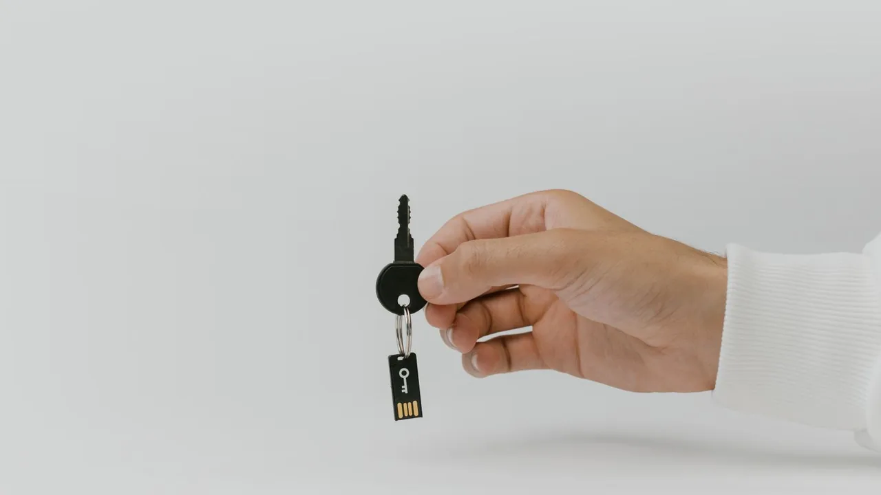 Une main tient une clé USB accrochée à un porte-clés, sur fond gris clair