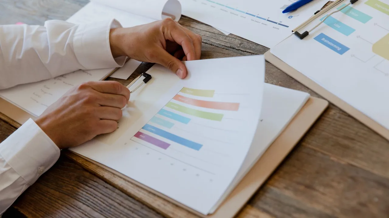 Des mains relisent un rapport imprimé avec des graphiques sur un bureau en bois
