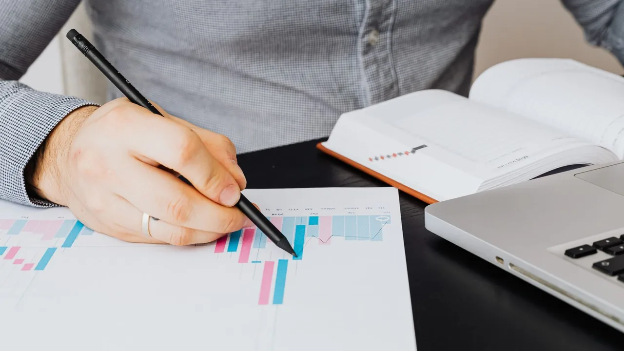 Un homme pointe un crayon sur un graphique imprimé, à côté d'un ordinateur portable et d'un carnet