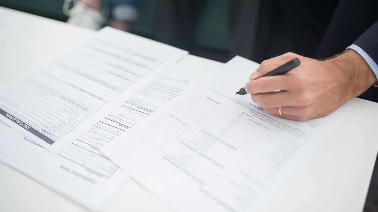 Gros plan d'une main qui signe un formulaire imprimé posé sur une table blanche.