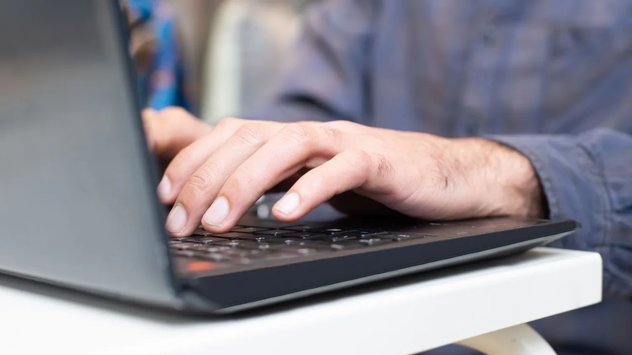 Mains d'un homme en chemise bleue tapant sur le clavier d'un ordinateur portable noir