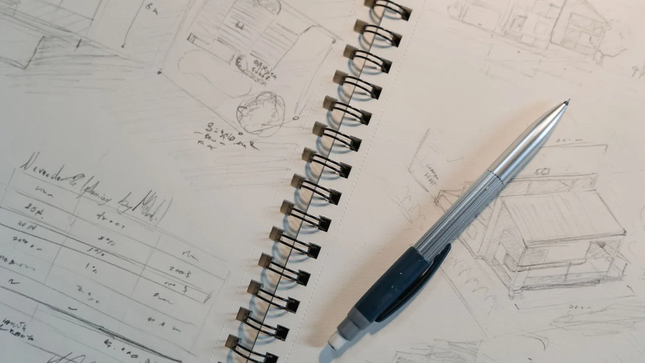 Un carnet à spirales ouvert sur des croquis au crayon, avec un stylo posé dessus