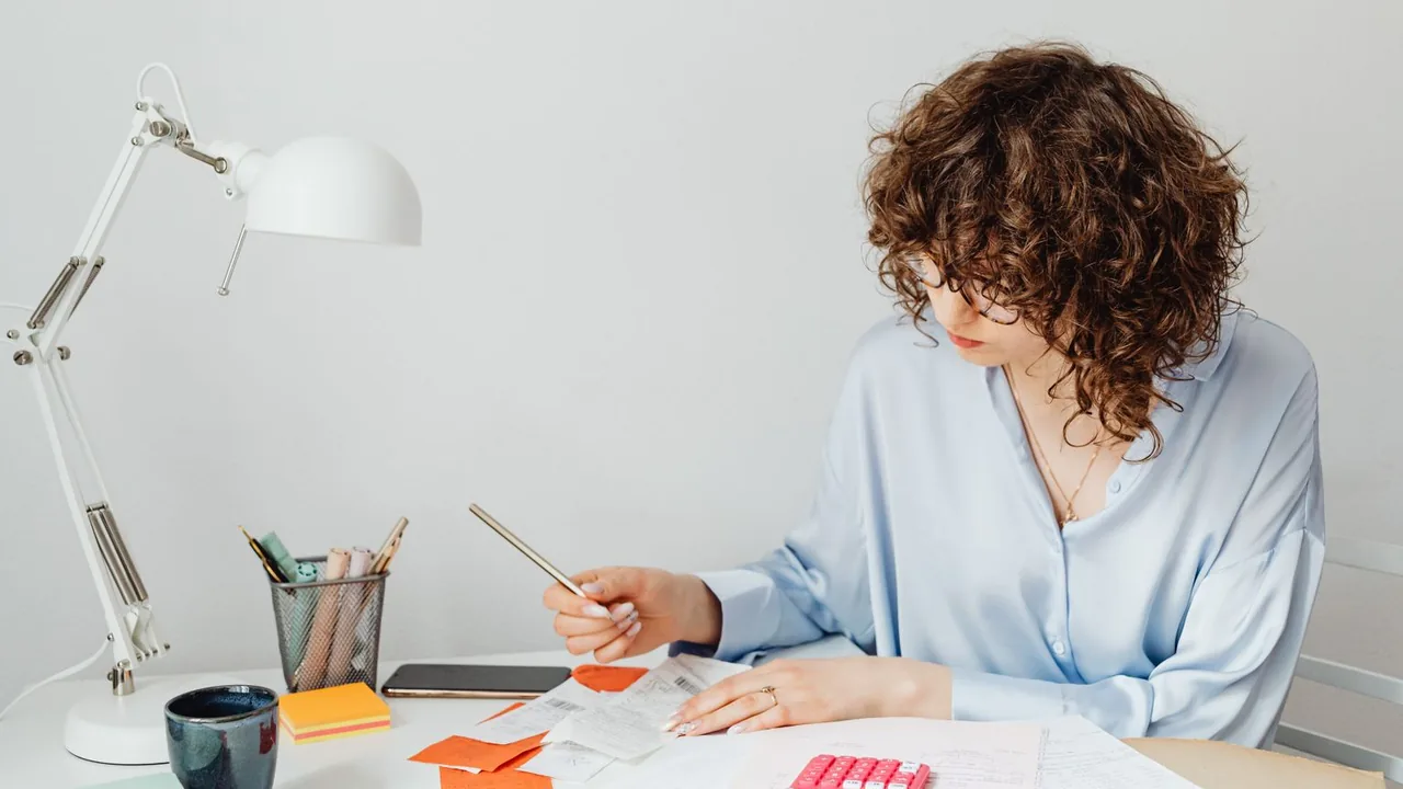 Une femme calcule des dépenses avec une calculatrice et des documents sur son bureau, un café à portée de main
