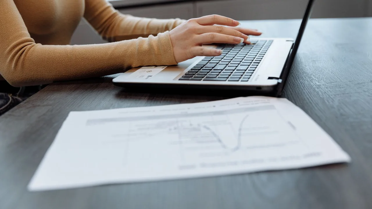 Mains sur le clavier d'un ordinateur portable, un document imprimé avec un graphique posé sur le bureau