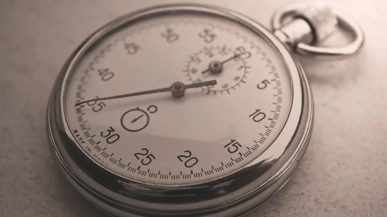Chronomètre mécanique ancien posé sur une surface grise, aiguilles et graduations visibles