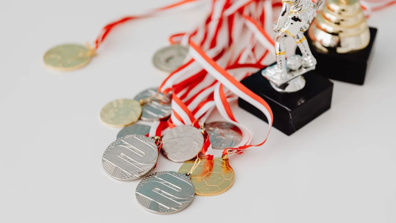 Médailles à rubans rouges et blancs et petits trophées posés sur une surface claire