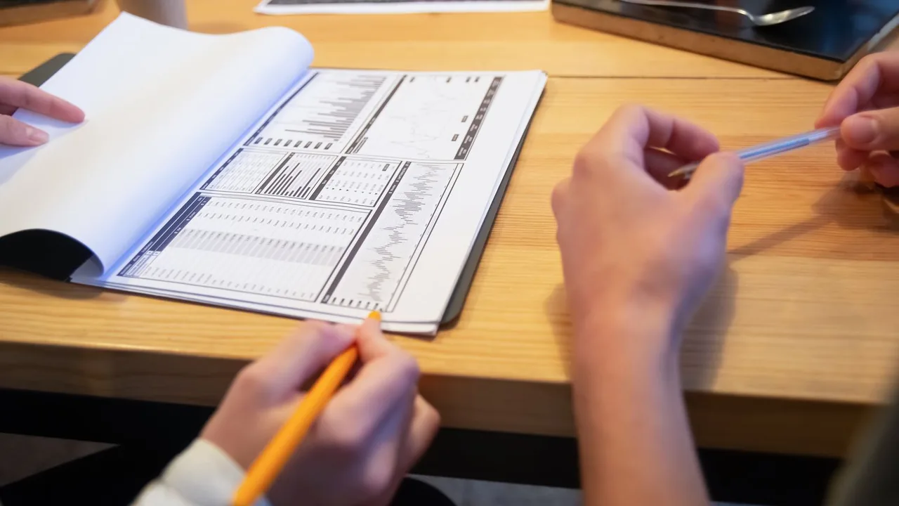 Mains de collègues qui commentent des tableaux d'analyse imprimés à l'aide de crayons, sur une table en bois