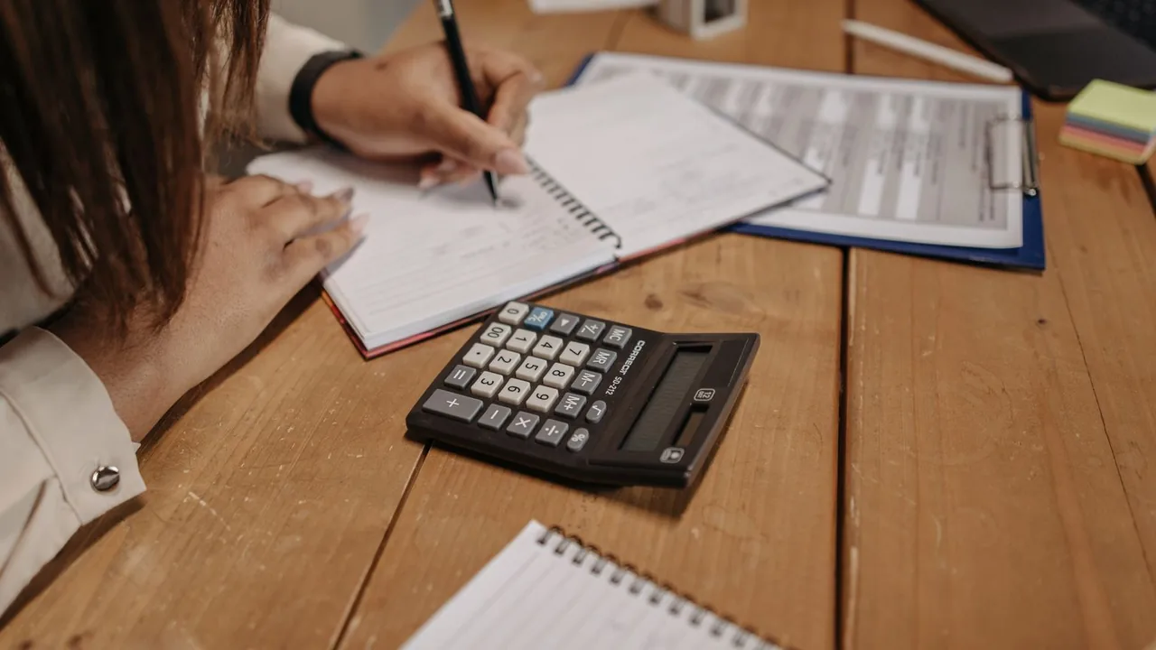 Une femme prend des notes sur un bureau en bois, une calculatrice à côté d'elle
