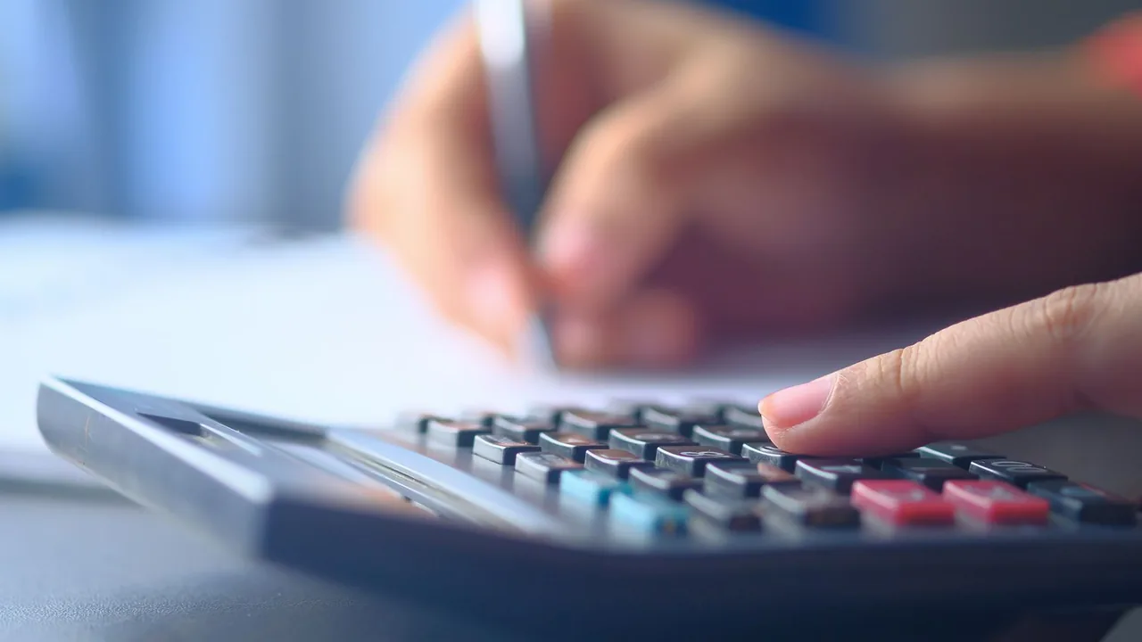 Gros plan sur des mains qui tapent sur une calculatrice et écrivent sur une feuille