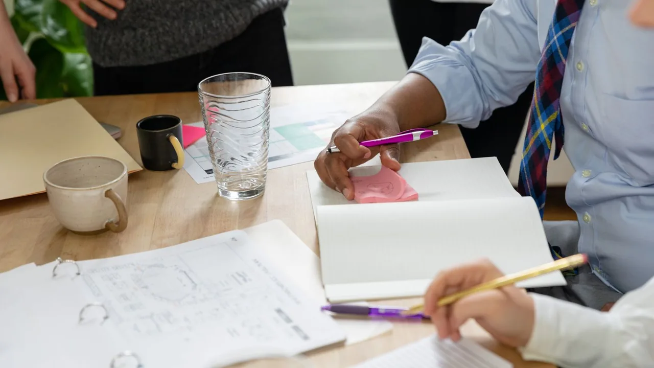 Mains prenant des notes dans des carnets autour d'une table avec un plan et des tasses