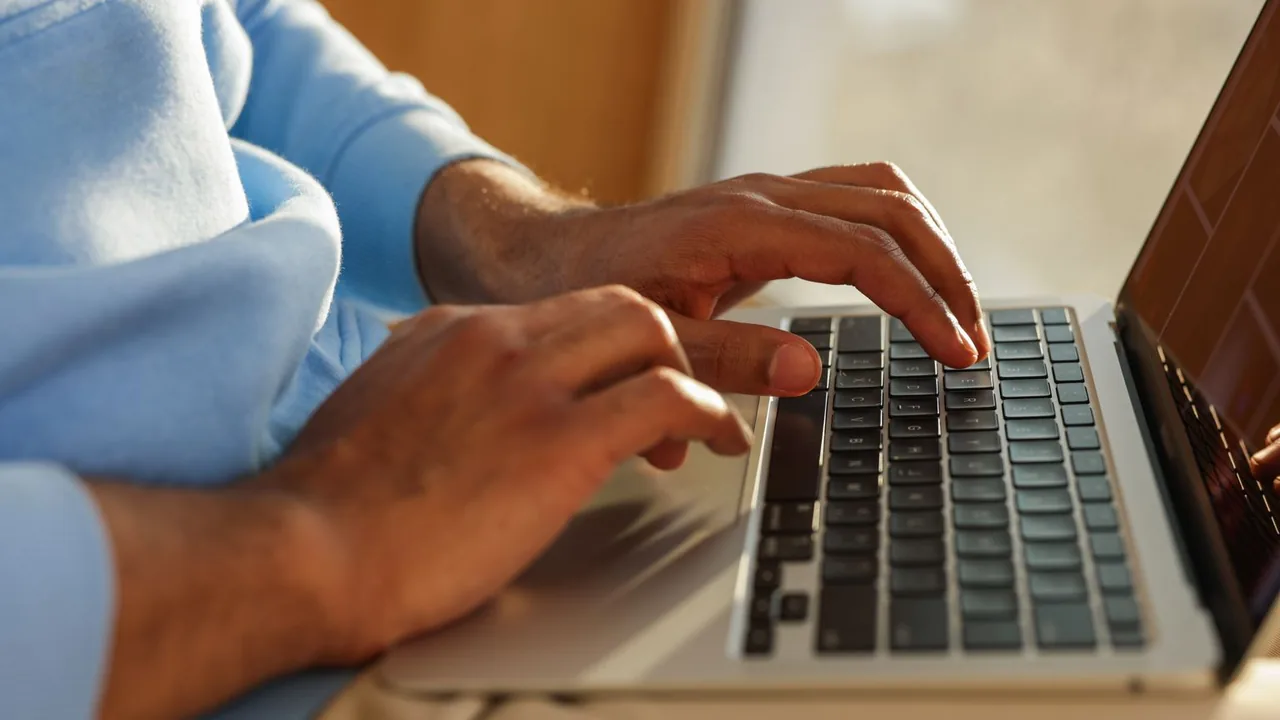 Mains d'un homme en pull bleu clair tapant sur le clavier d'un ordinateur portable, lumière chaude