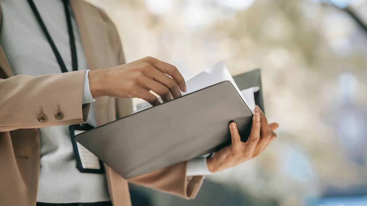Les mains d'une femme tiennent un dossier dont elle sort des documents