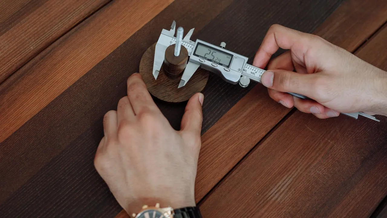 Des mains mesurent une pièce en bois avec un pied à coulisse numérique sur une table