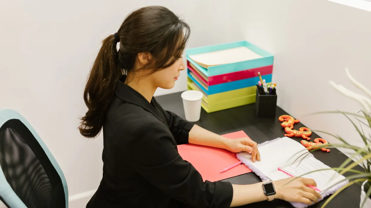 Une femme écrit dans un carnet à son bureau, près d'une pile de bacs de rangement colorés