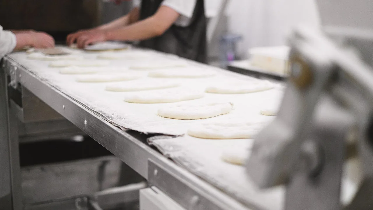 Des boulangers façonnent des morceaux de pâte alignés sur un tapis de production