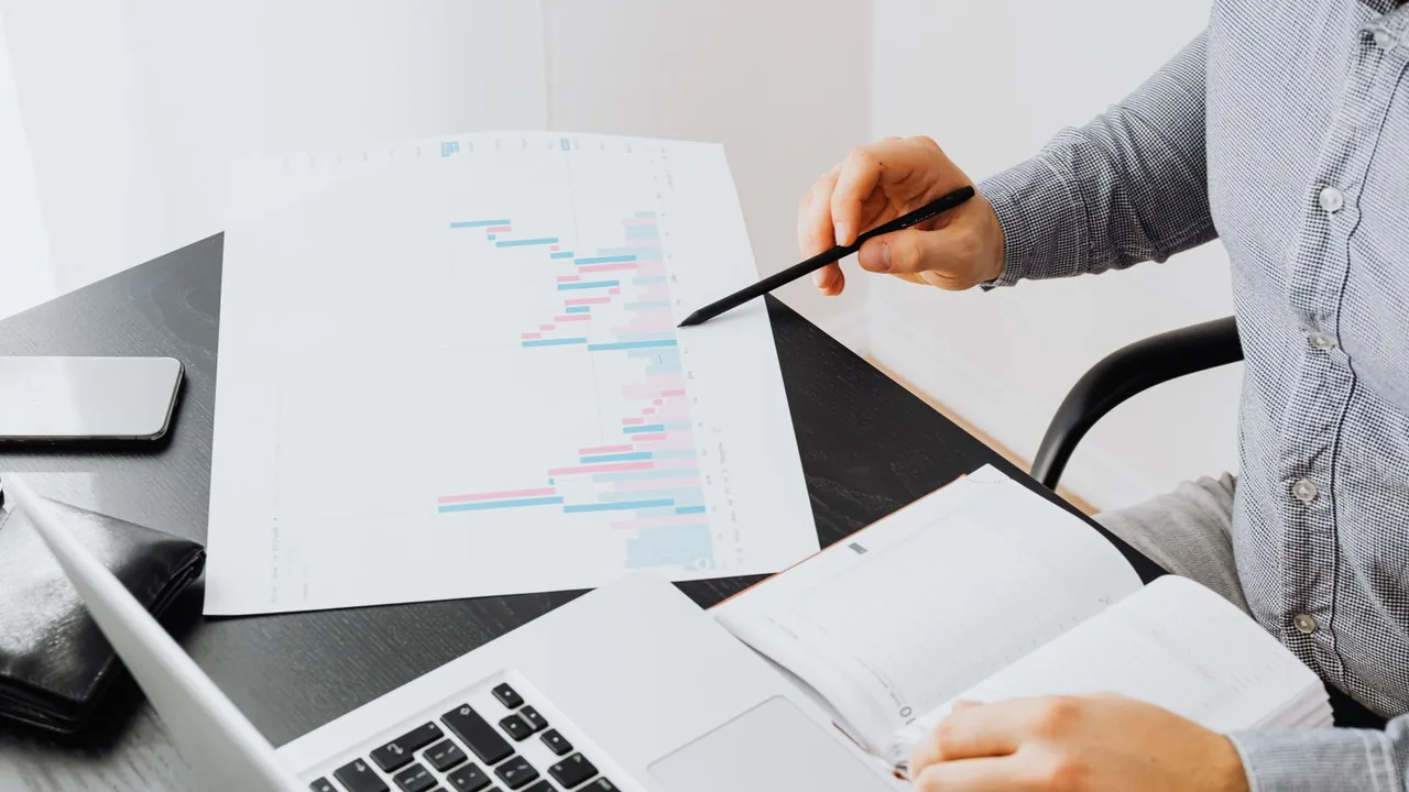 Personne pointant un graphique imprimé à côté d'un ordinateur portable sur un bureau