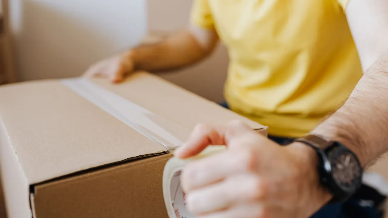 Mains fermant un carton avec du ruban adhésif sur une table