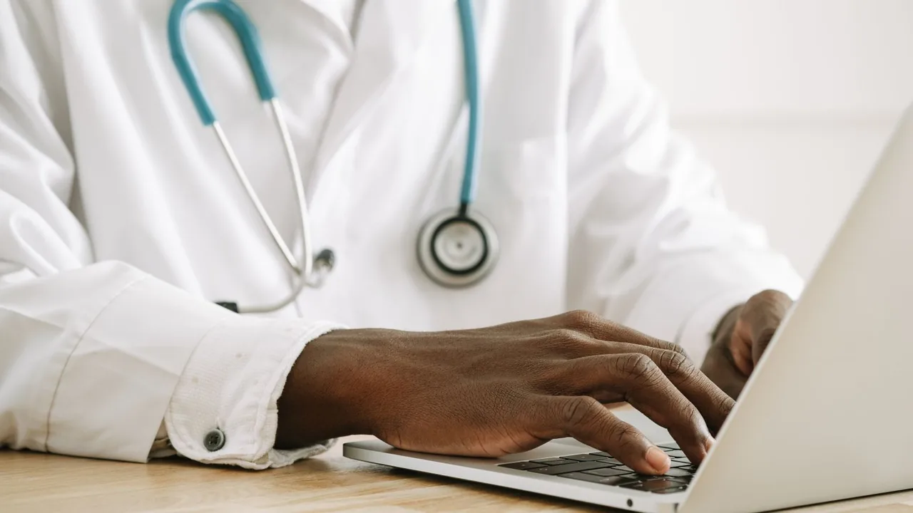 Les mains d'un médecin en blouse blanche tapent sur un ordinateur portable, stéthoscope autour du cou