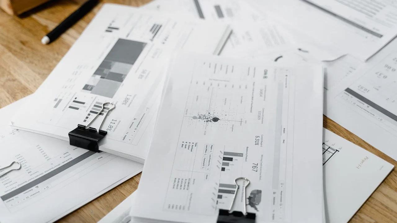 Une pile de rapports financiers et de graphiques tenus par des pinces, posée sur un bureau en bois.
