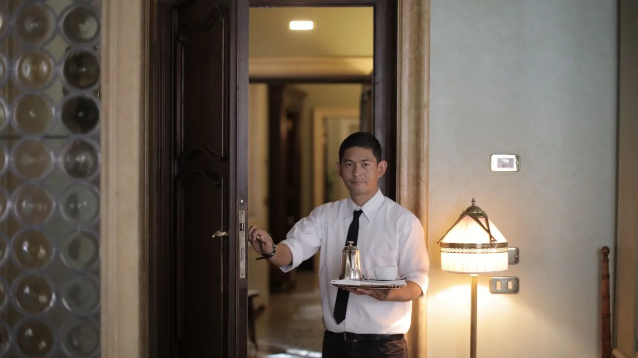 Serveur en chemise blanche ouvrant la porte d'une chambre avec un plateau de service