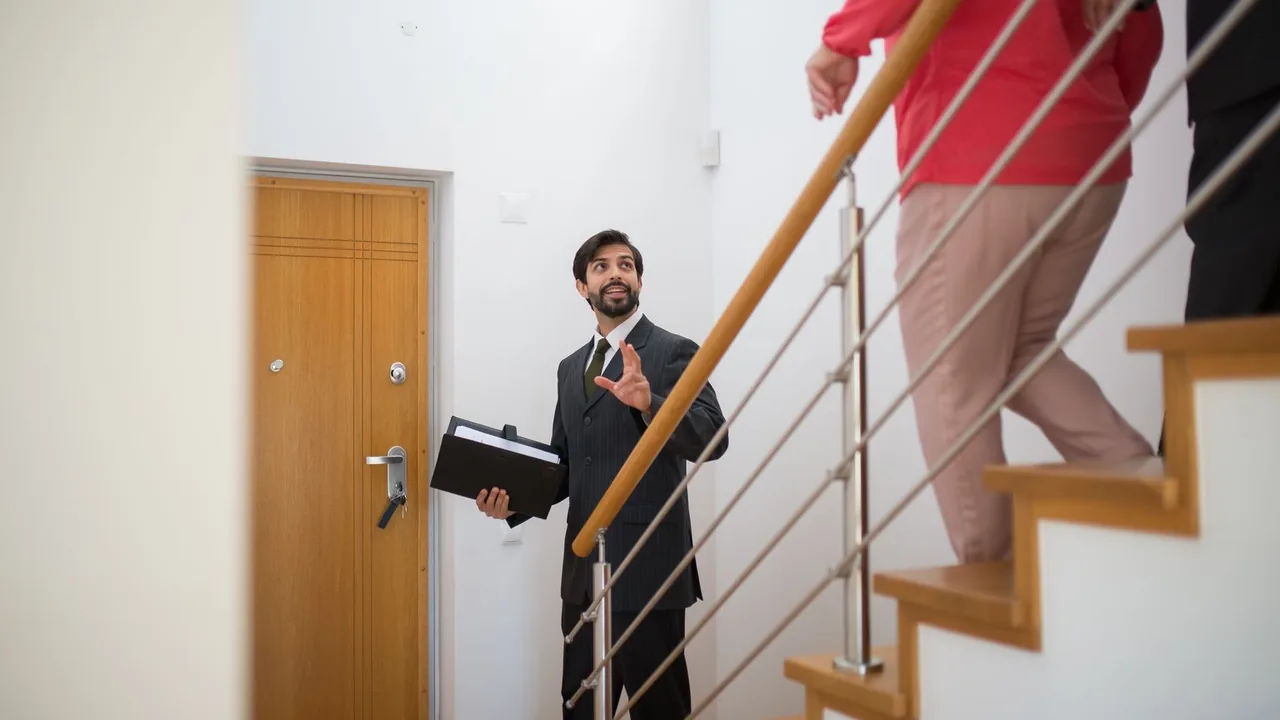Un agent immobilier avec un dossier sous le bras guide des visiteurs dans l'escalier d'un logement