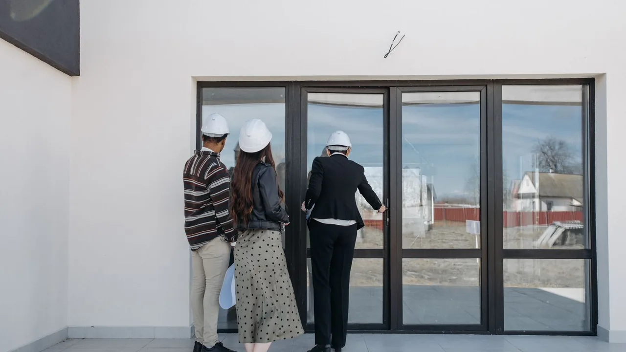 Trois personnes casquées, vues de dos, regardent par la grande baie vitrée d'un logement en construction