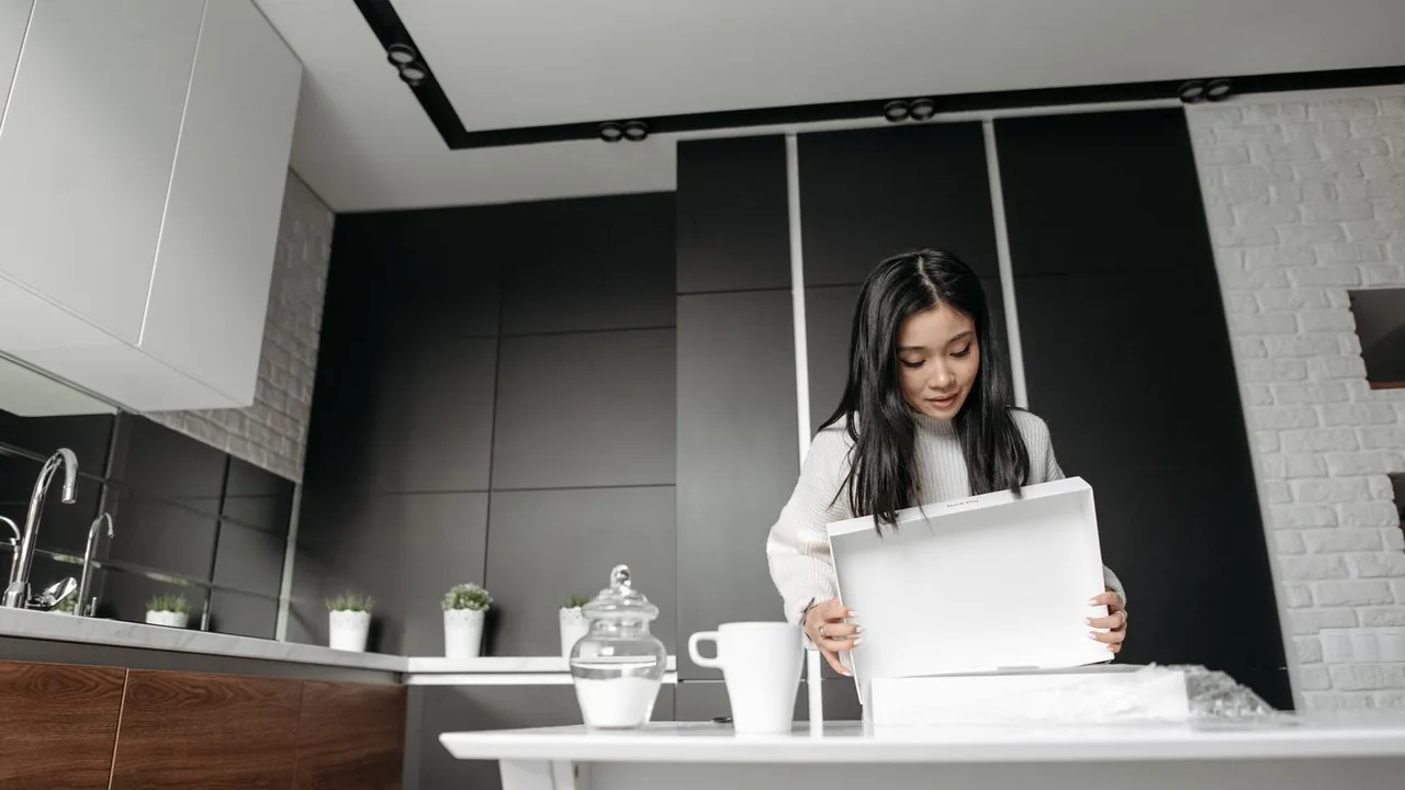 Une femme déballe un colis dans une cuisine moderne aux meubles sombres