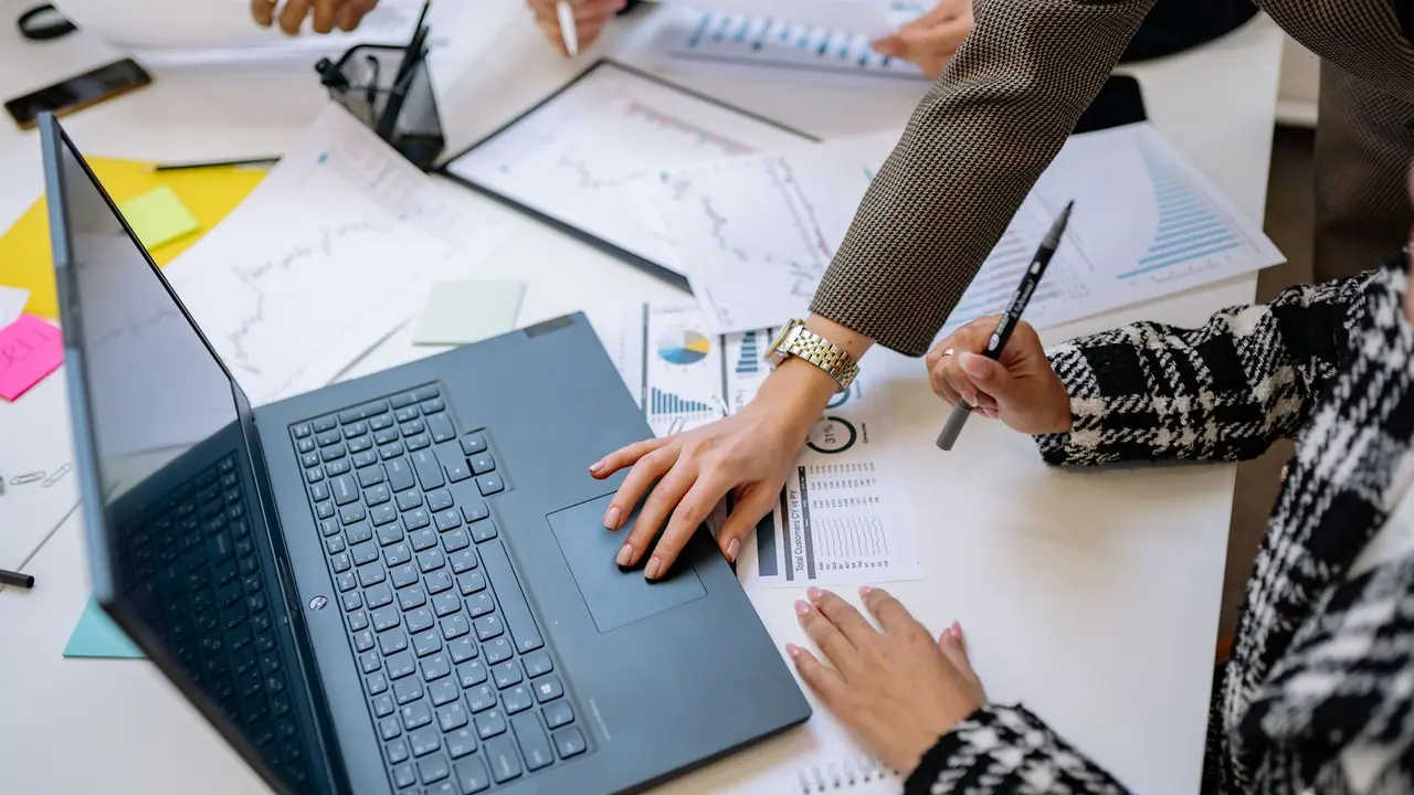 Une équipe analyse des documents et des graphiques autour d'un ordinateur portable posé sur la table.