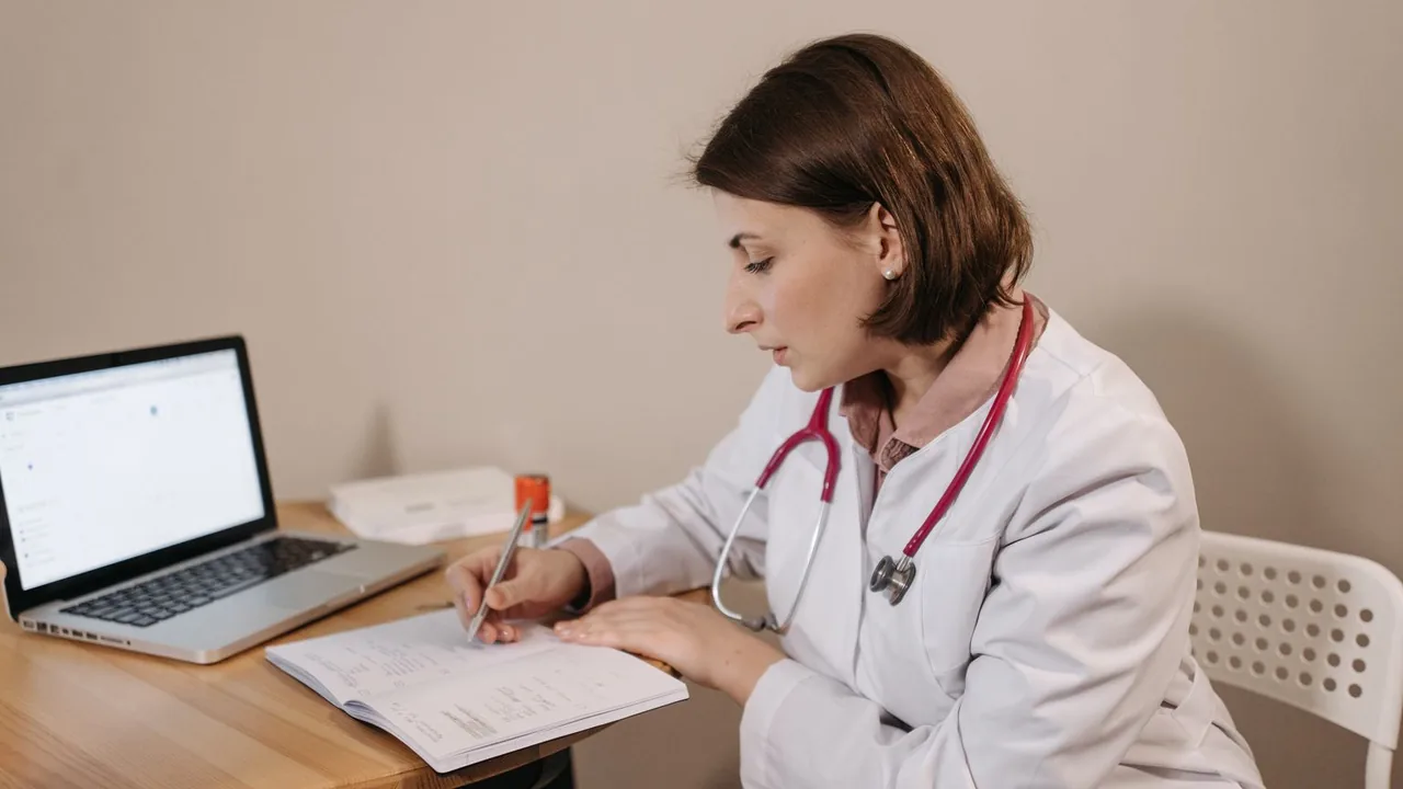 Une médecin en blouse blanche, stéthoscope autour du cou, écrit dans un cahier à côté d'un ordinateur portable