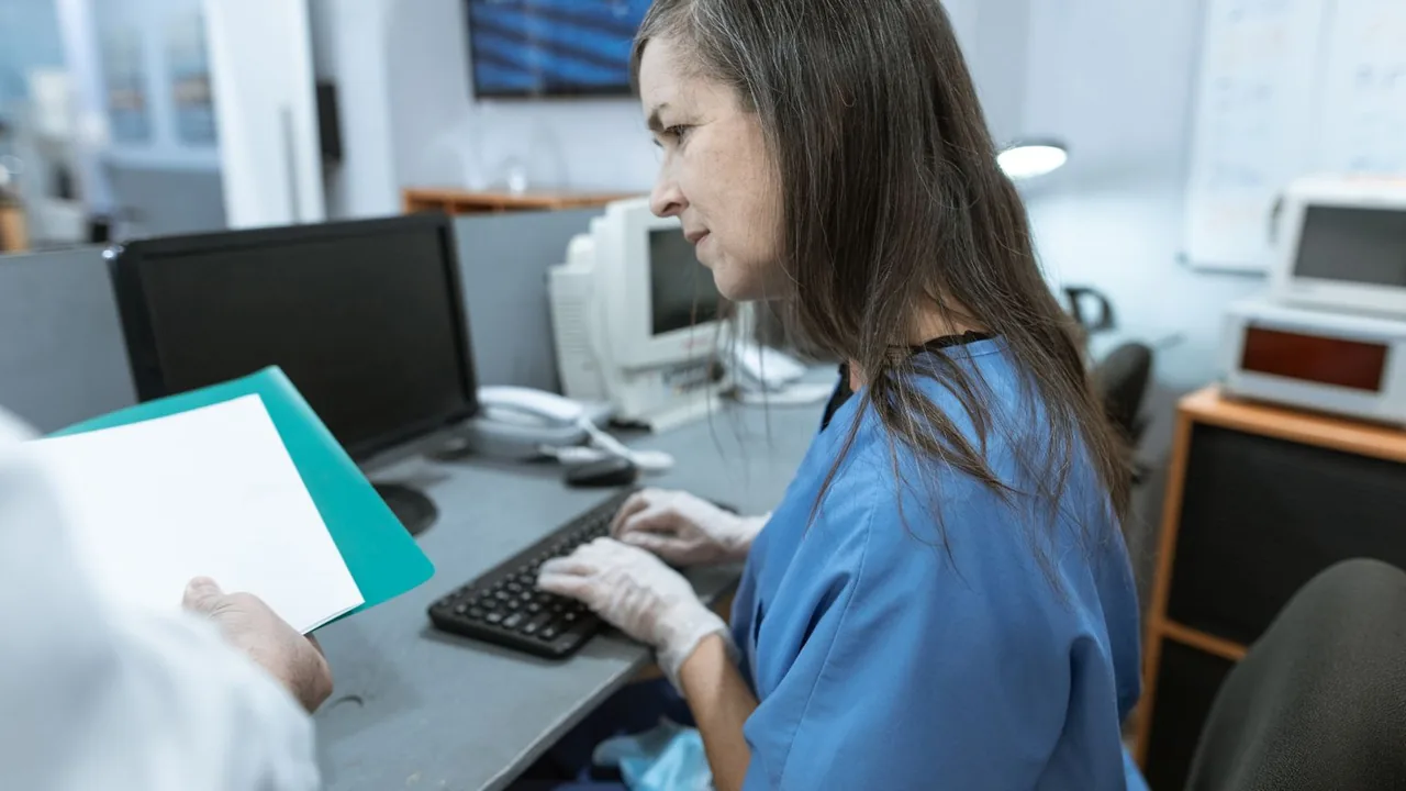 Une infirmière en blouse bleue saisit des données au clavier d'un poste de travail de l'hôpital