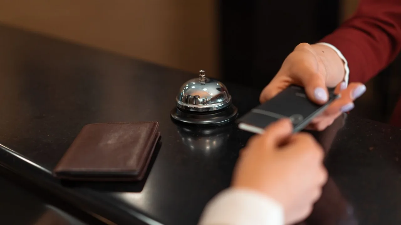 Les mains d'un client et d'une réceptionniste échangent une carte devant la sonnette d'un comptoir d'hôtel