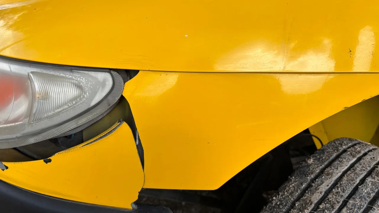 Gros plan sur l'aile avant d'une voiture jaune enfoncée près du phare après un choc