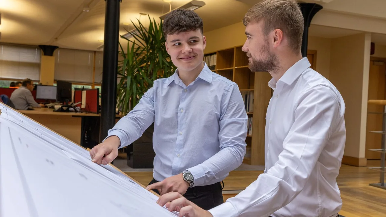 Deux collègues penchés sur de grands plans dans un bureau ouvert