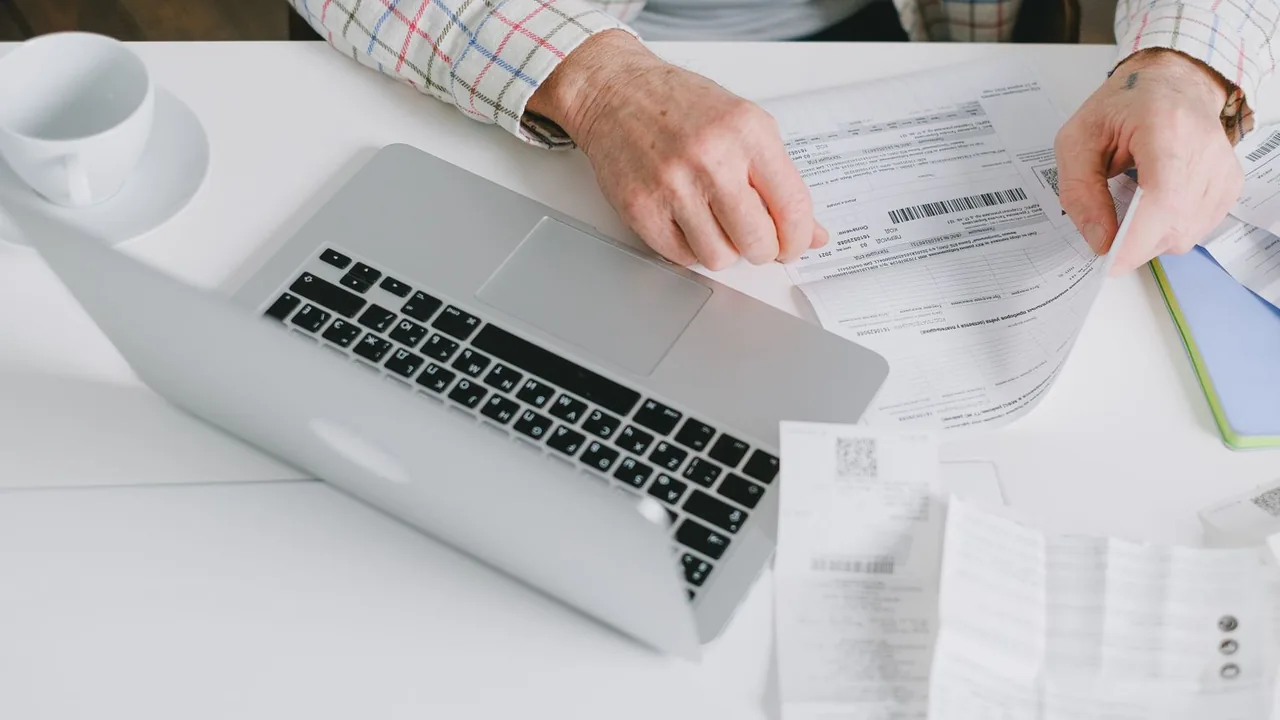Gros plan de mains qui trient des documents posés sur un bureau devant un ordinateur portable