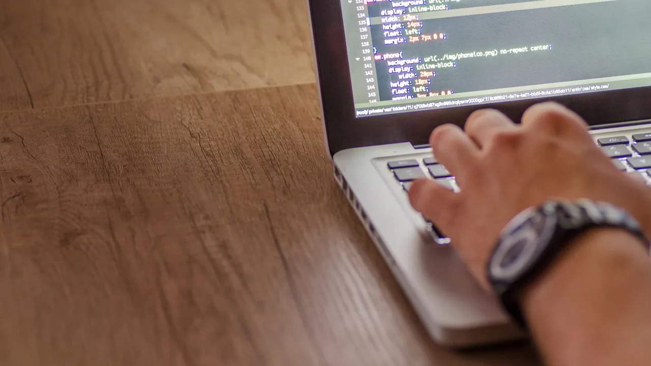 Gros plan sur une main qui tape sur le clavier d'un ordinateur portable posé sur un bureau en bois