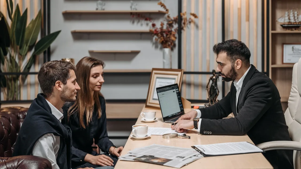 Trois professionnels discutent à une table de bureau, un ordinateur portable ouvert devant eux