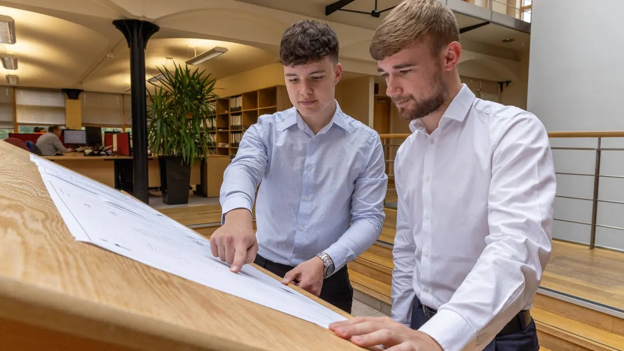Deux jeunes collègues examinent un plan posé sur une table haute dans un bureau